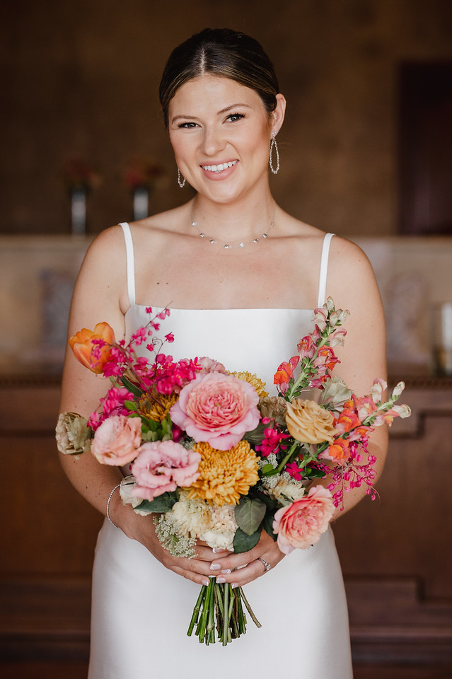 Smiling bride holding a vibrant and colorful wedding bouquet with pink, orange, and yellow flowers. Custom Wedding Floral Designs tailored to your style.