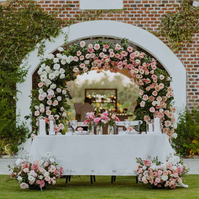 Elegant outdoor wedding reception table in Los Cabos with pink and white floral centerpieces and string lights. About Our Story at Del Mar Floristería.